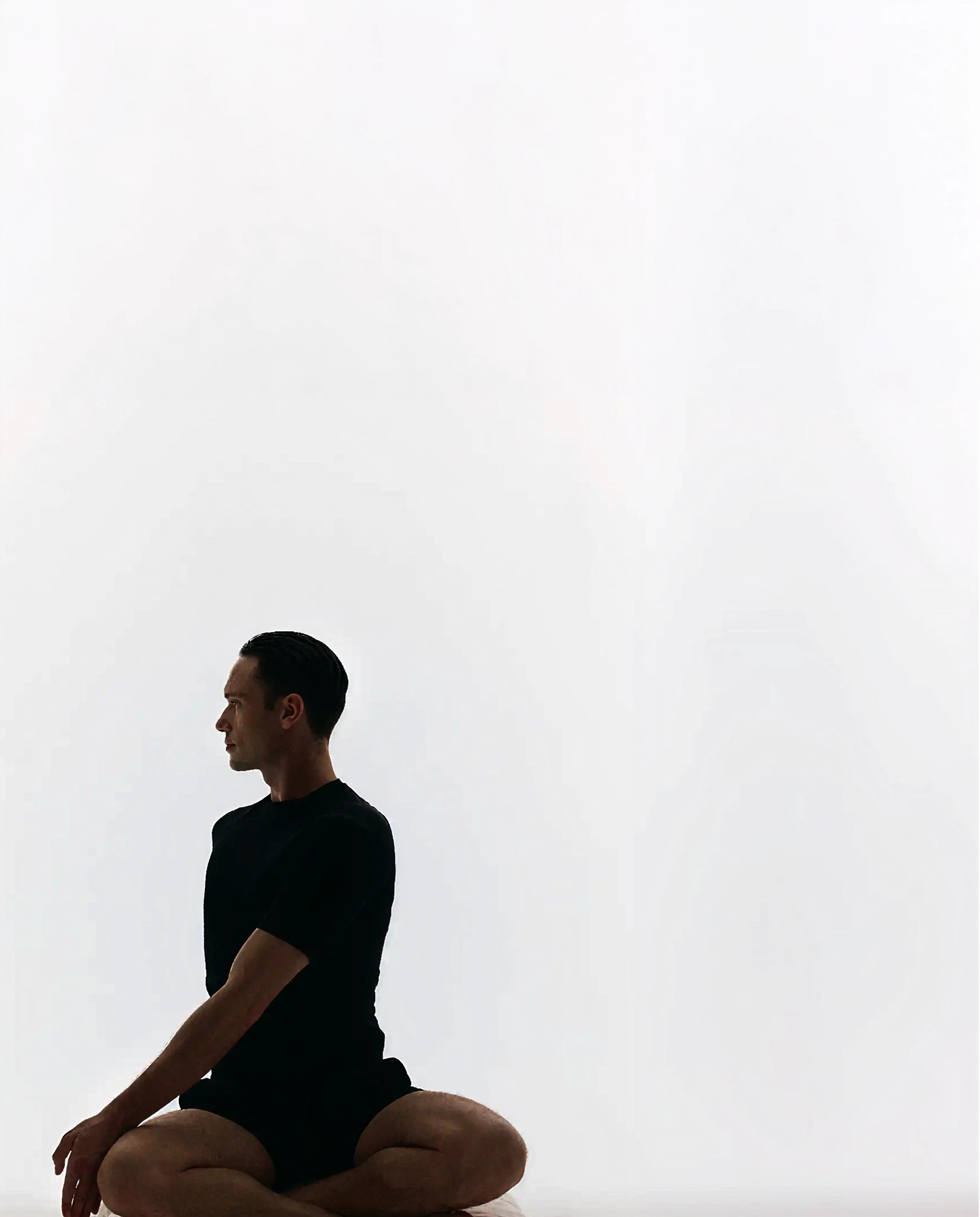 A man sitting cross-legged in profile against a light studio backdrop